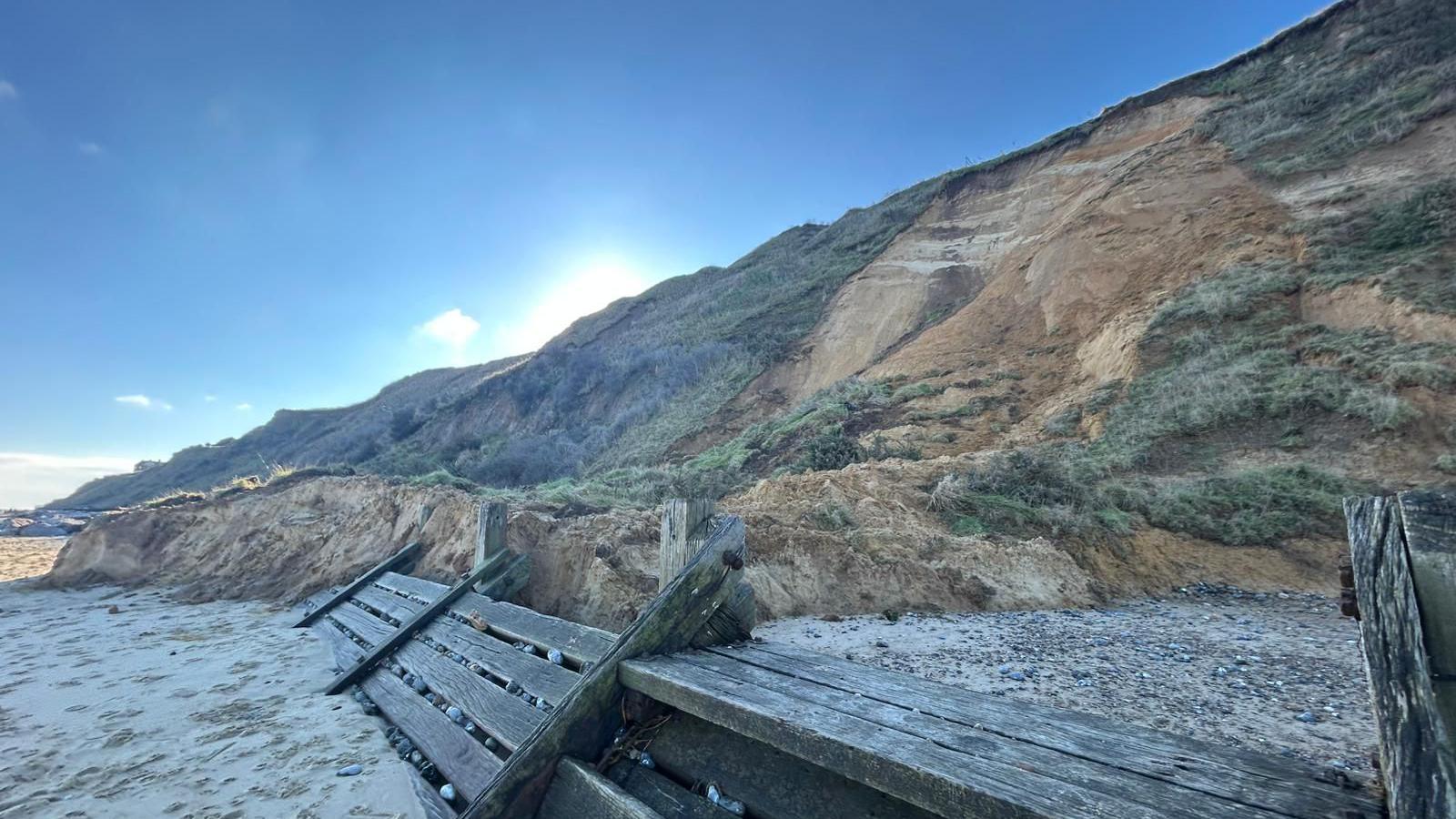 Parts of a cliff are now on the sand after falling. There are wooden structures on the beach