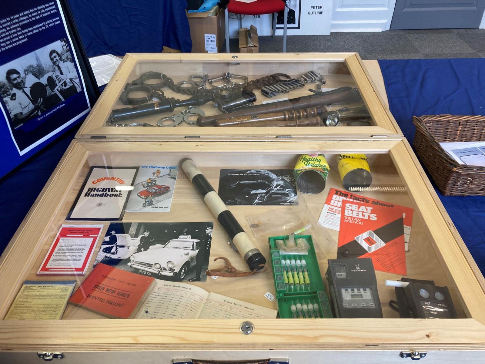 A glass case containing truncheons, handcuffs and road safety booklets.