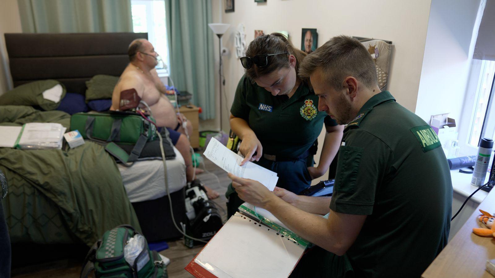 Two paramedics visit a middle aged man who is struggling to breathe. He has an oxygen mask on while the paramedics check his notes