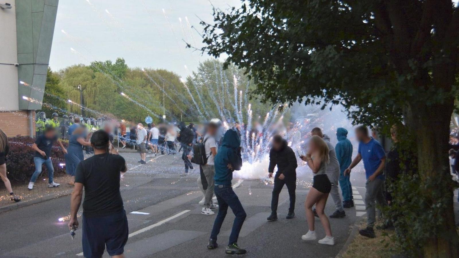 A small crowd of protesters are turning away as a firework exploded in the car park of the Holiday Inn Express. The corner of the hotel building can be seen a few metres away.