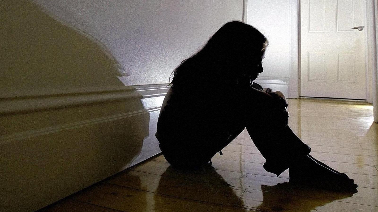 A silhouette of a girl sitting in a hall way.