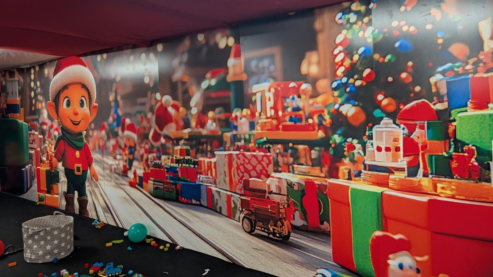 A Christmas toy-themed wall. It shows wrapped presents, Christmas trees and baubles, as well as an elf wearing a Christmas hat on the left side.