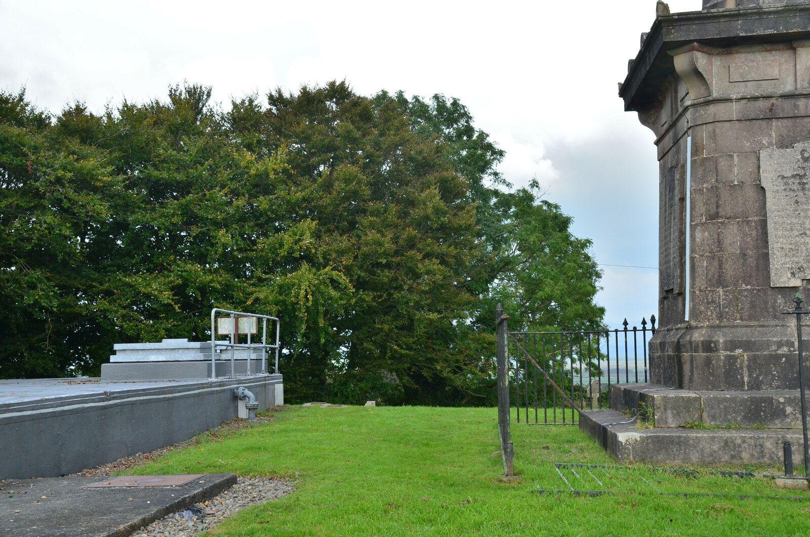 The side of a water tank next to a large stone monument separated by a few yards of grass