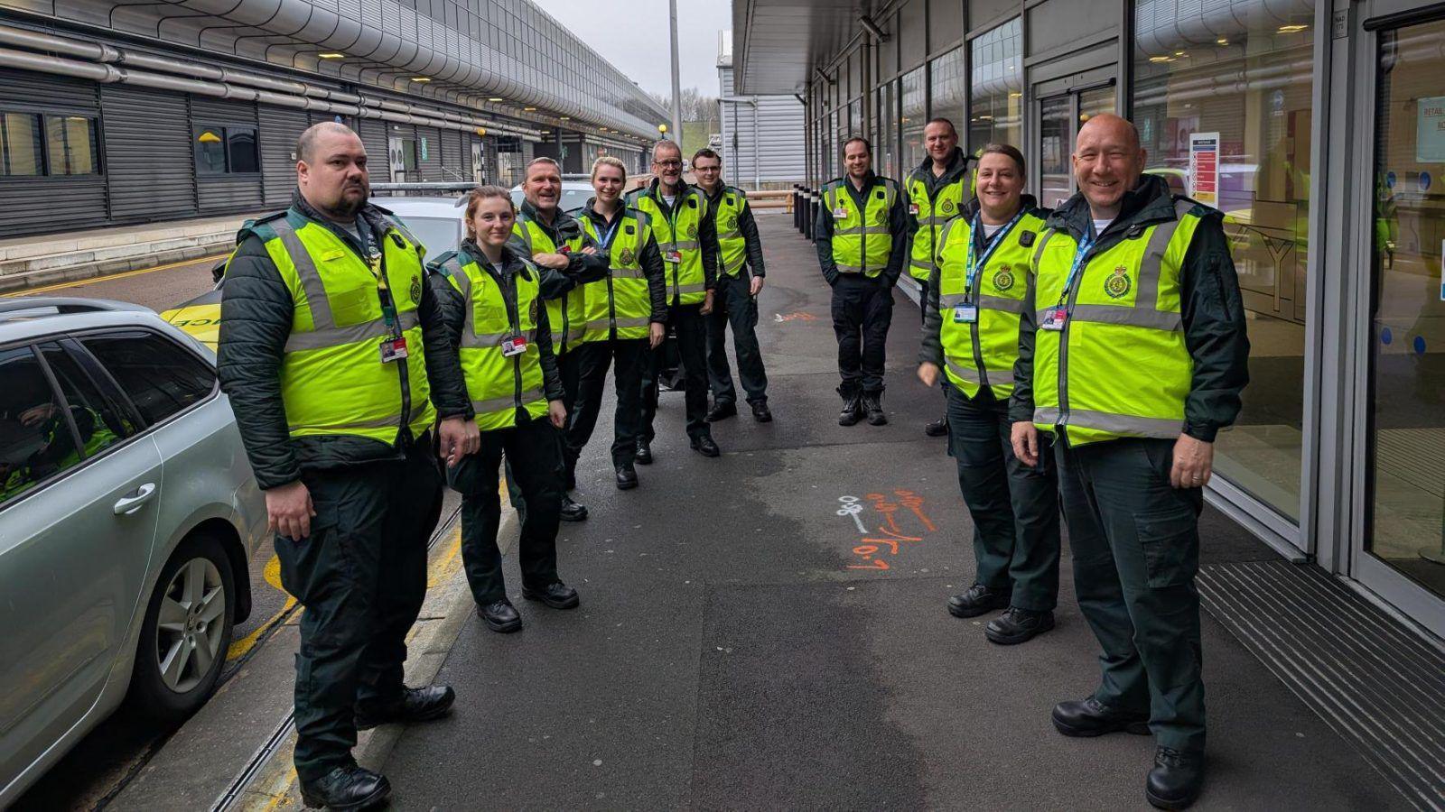 Members of Secamb staff stand outside Gatwick Airport in yellow hi-vis jackets and green uniforms