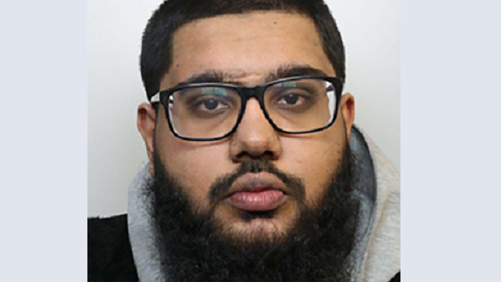 A custody image of Faseh Sajid. He is looking at the camera wearing glasses and has a beard. He is wearing a grey hoodie