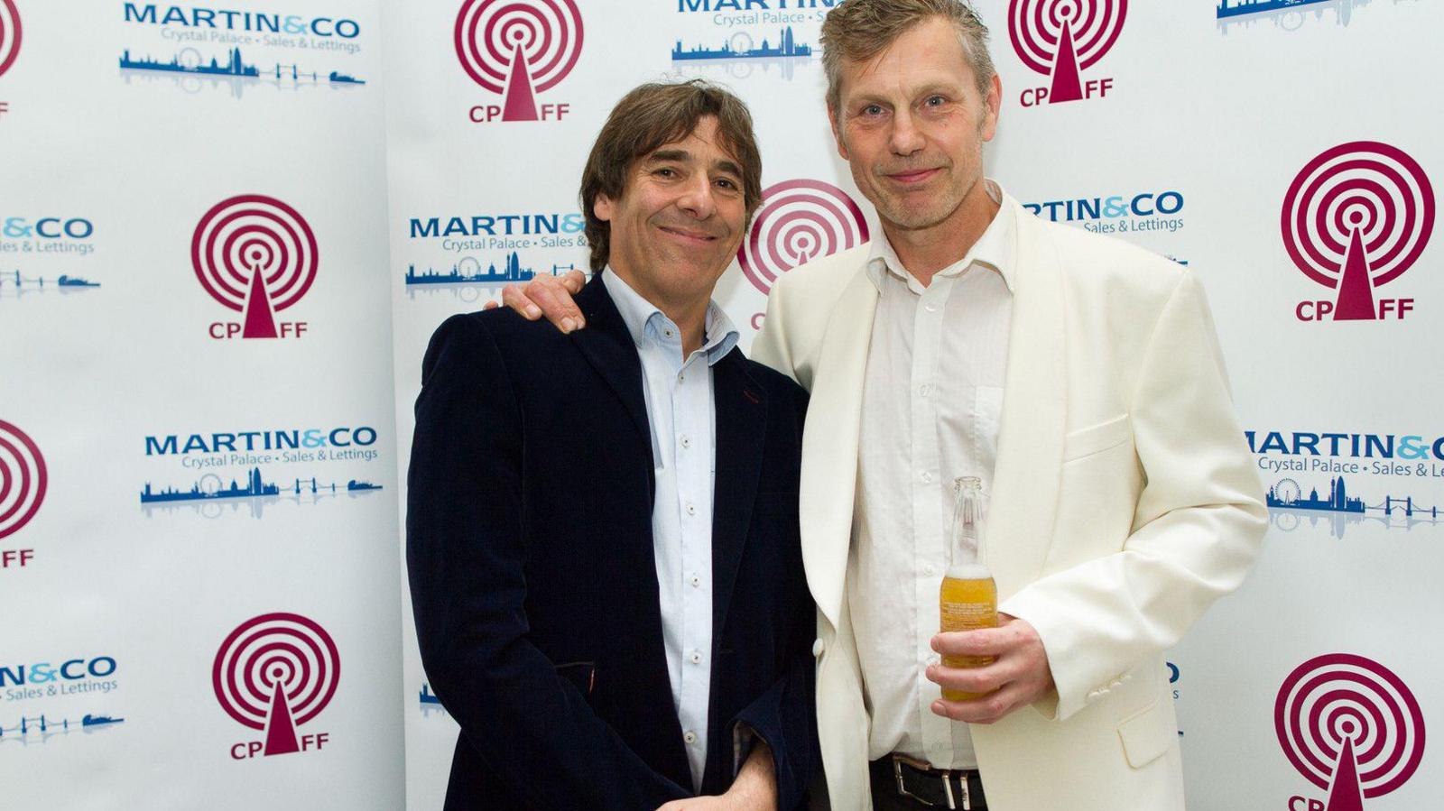 Comedian Mark Steel, a man in a black suit and light coloured shirt, with Neill Roy, right, wearing a white/cream coloured suit