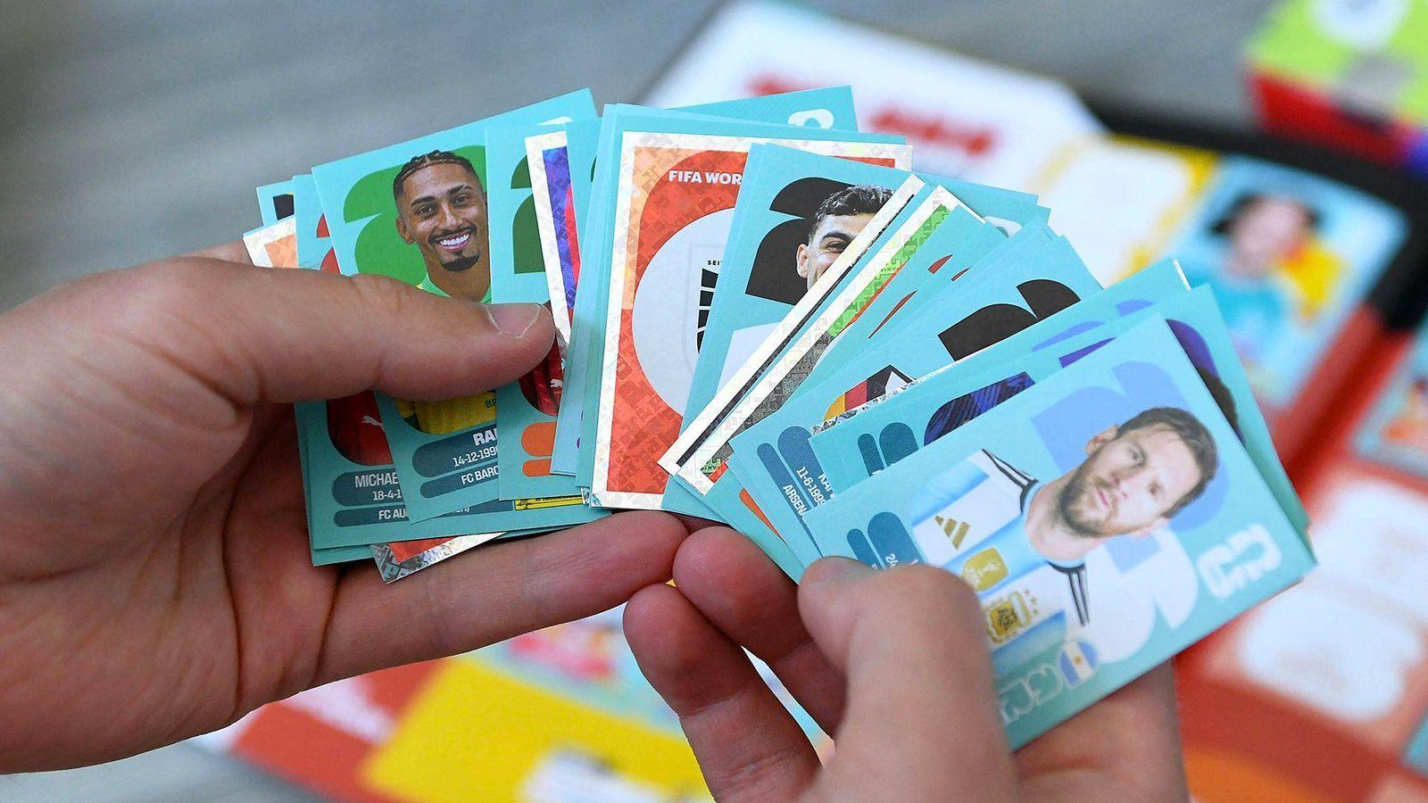 A number of football player stickers held in a messy fan in someone's hand, with a blurred background showing the album on a table.