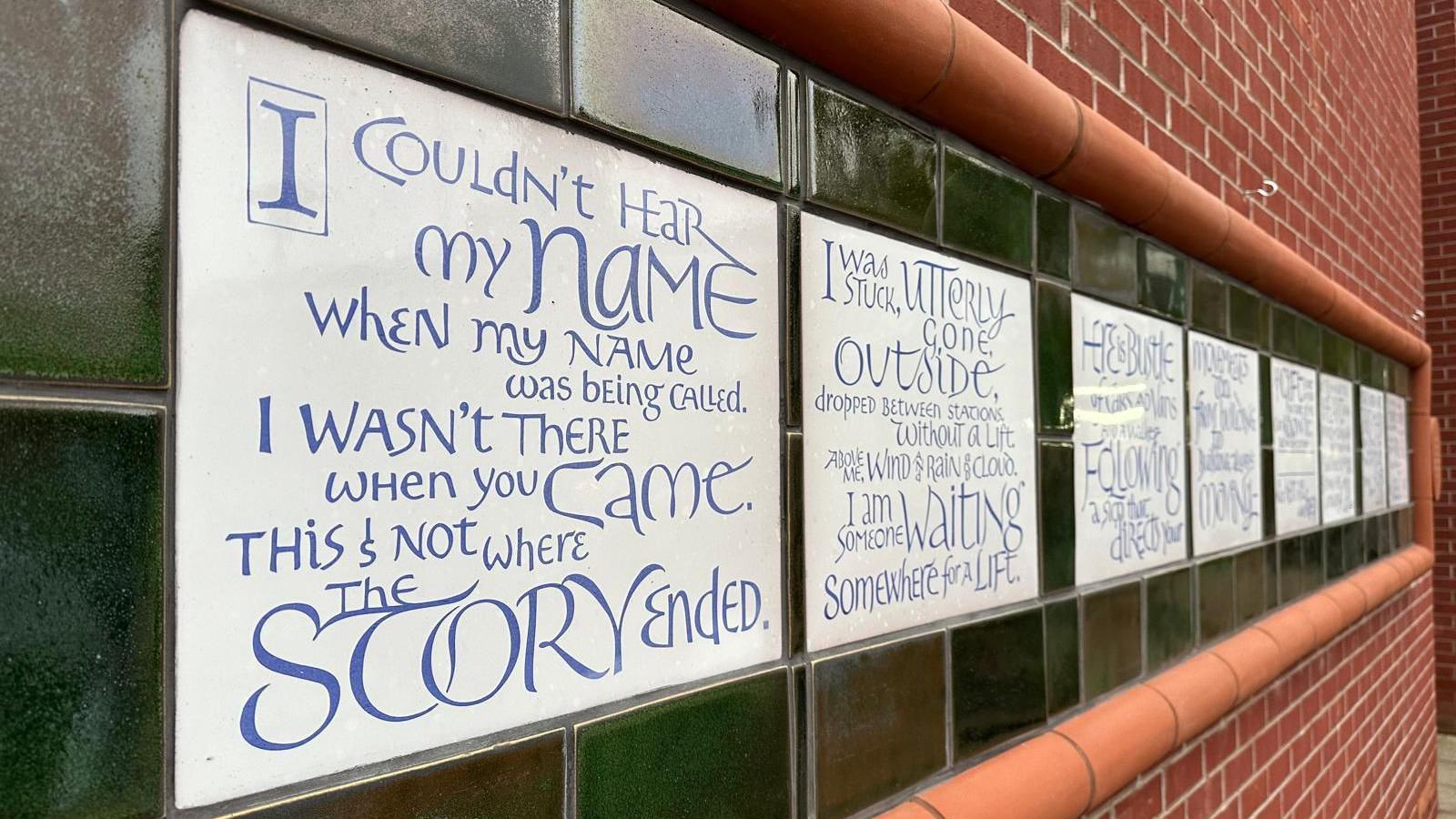 A side view of the mural, which features white ceramic panels covered with the words of the poem 'The Call' 