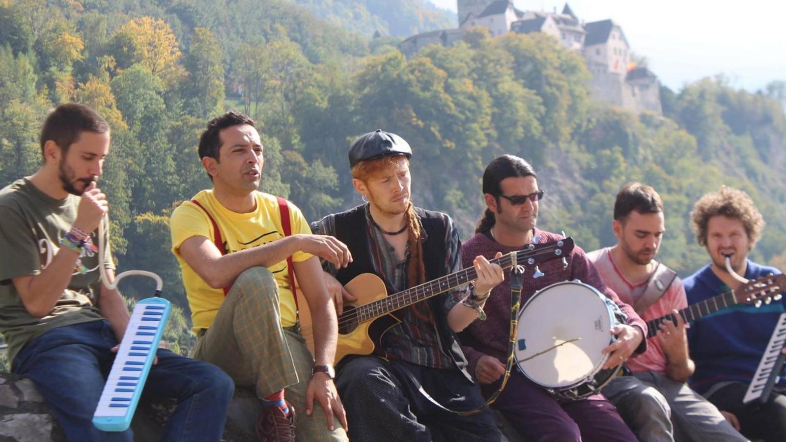 Opaque are sat on a wall with trees, hills and a large castle like building in the distance behind them. All band members, apart from Moony are holding instruments. Two have melodicas, keyboards with tubes to blow into, two have guitars and another has a drum. 