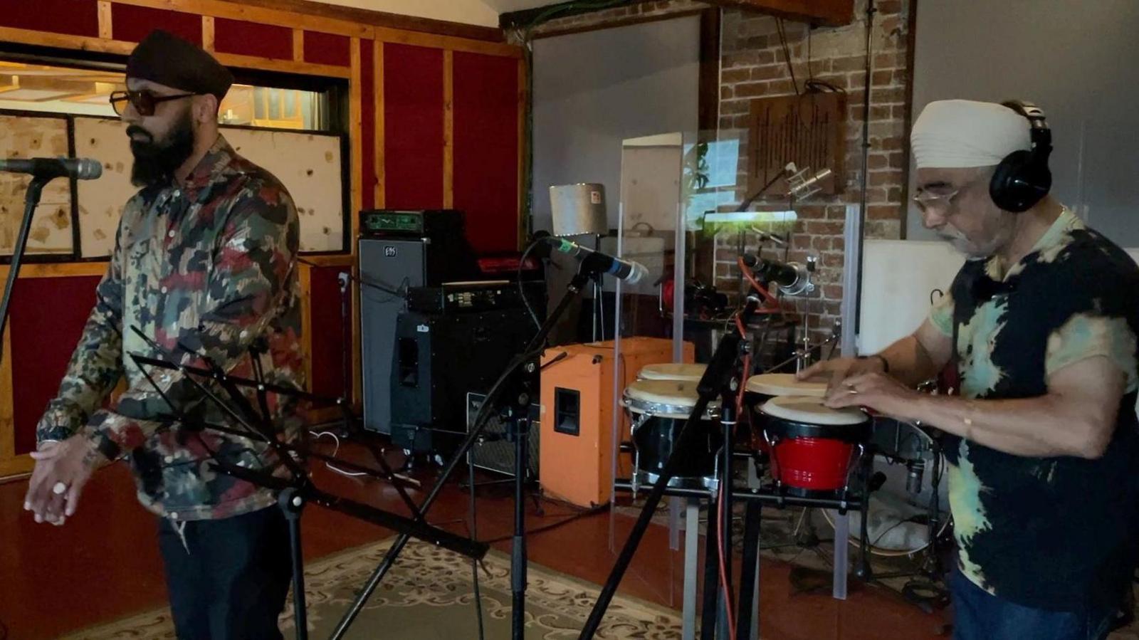 SilverFinger Singh, on the left, singing into the mic and Inder Goldfinger playing drums on the right. They are both in the studio practising their set for their set at Dialled In, Summer Sounds event in Bradford. 