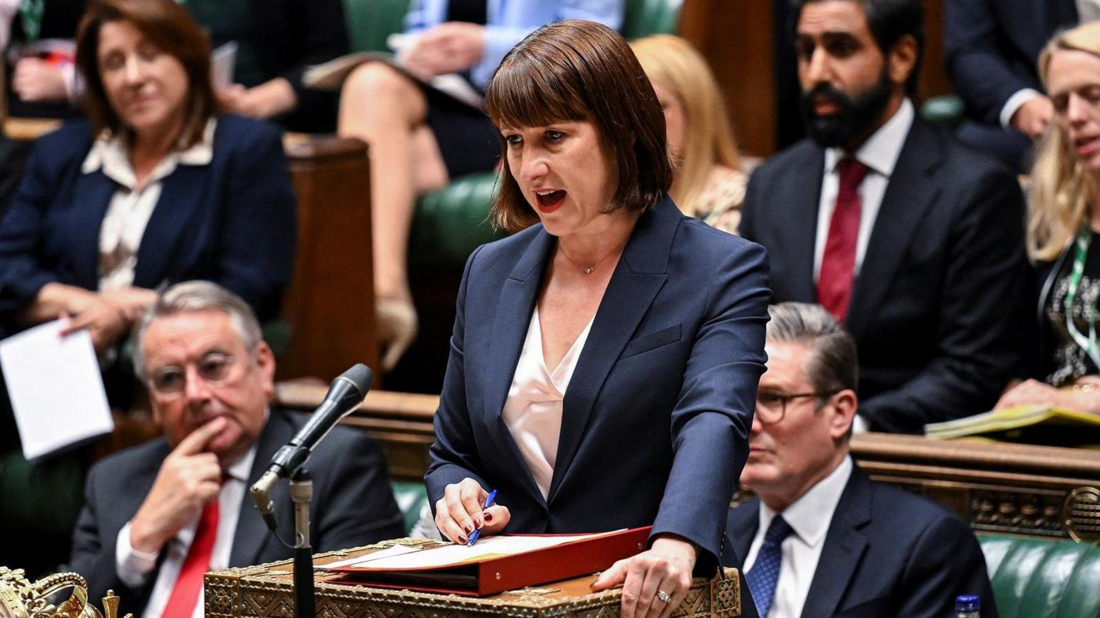 Chancellor Rachel Reeves stands and makes a speech in the House of Commons with Labour MPs, including Sir Keir Starmer, sitting on the green benches behind her