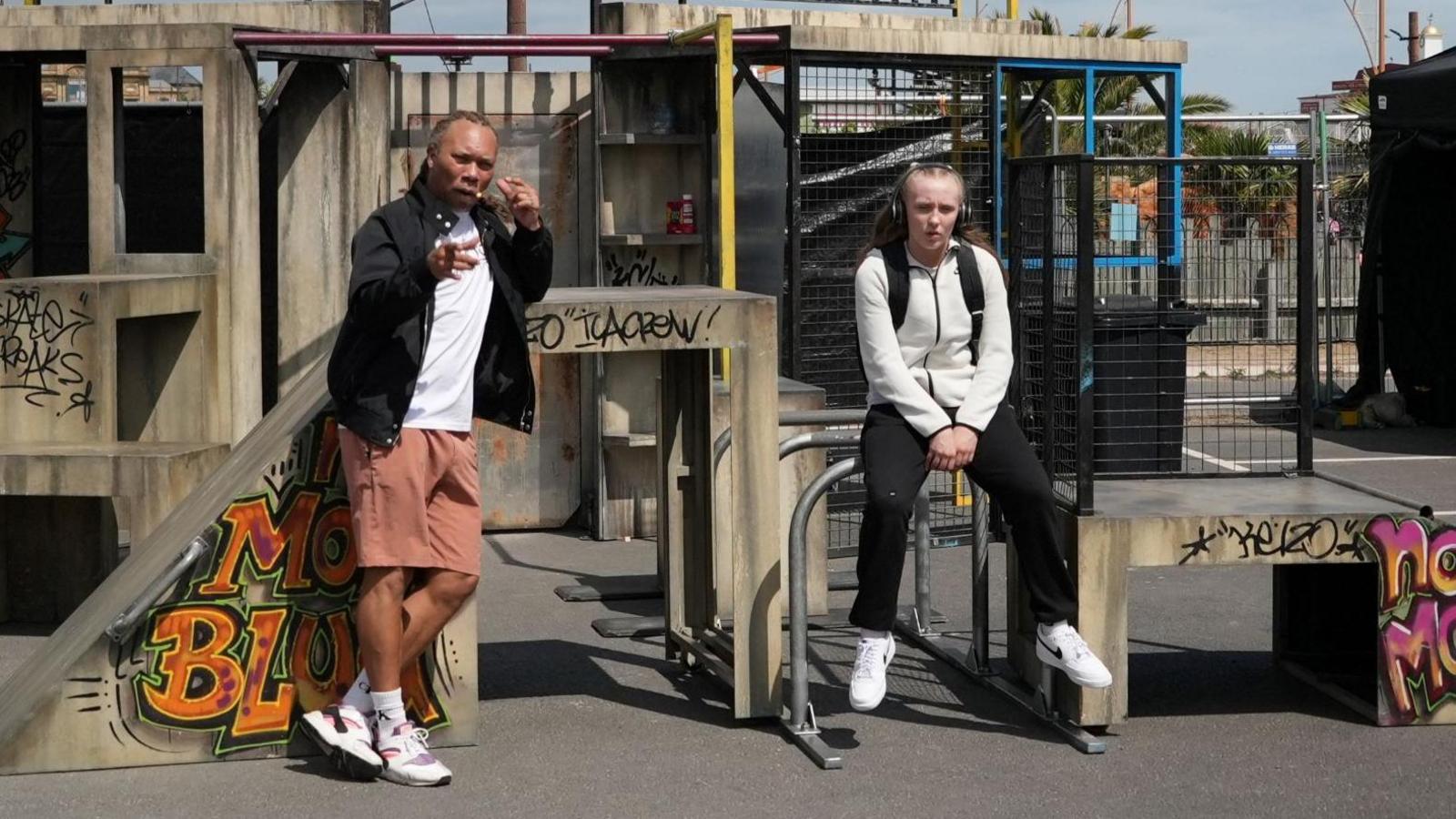 Two people sitting in a park. They are sitting on the apparatus and there is graffiti in the park.