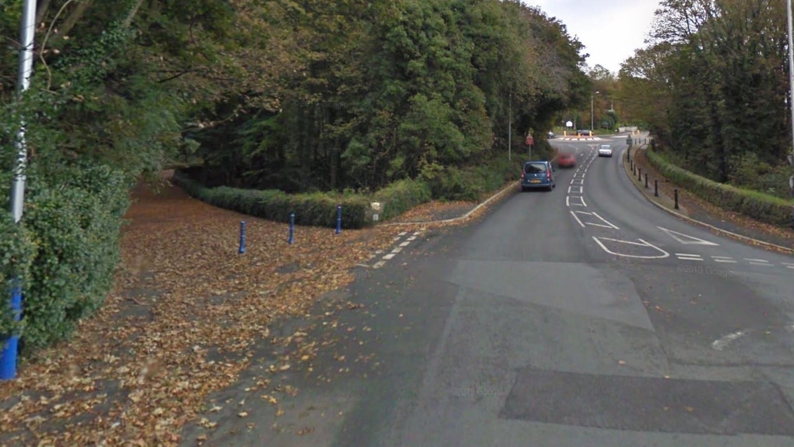 The turn off for Governor's Dip at the Victoria Road junction on the A2. The road is covered with leaves and there are blue traffic bollards in place. The road in front stretches out towards another roundabout at Governor's Road and there are trees lining either side of the carriageway.