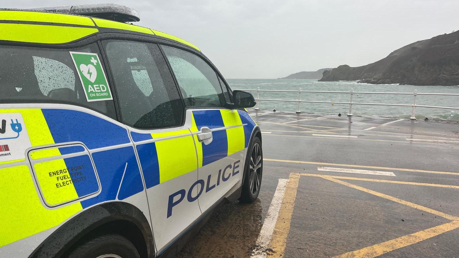 A States of Jersey Police car in a car park space in Greve de Lecq on a gloomy and rainy day with the sea looking choppy in the distance.