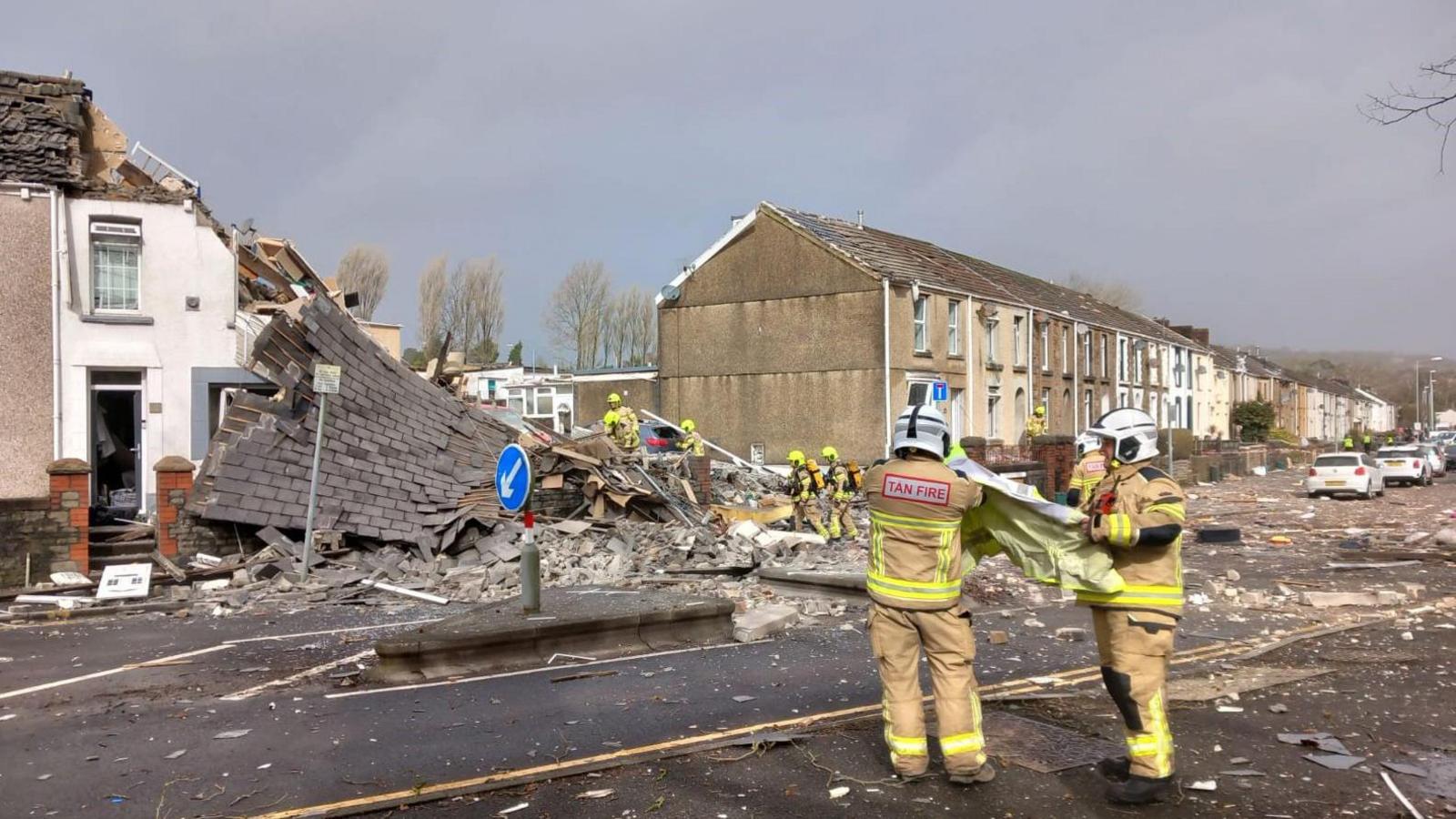 Emergency personnel at the scene after reports of a suspected gas explosion at a property on the junction of Clydach Road and Field Close in Morriston, Swansea. Behind them the rubble and remains of the house that was flattened, debris is scattered across the road.