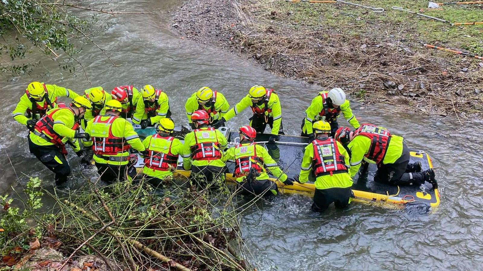 Fourteen people all wearing high-vis jackets are seen with an inflatable sled on a river, transporting Nicky the donkey