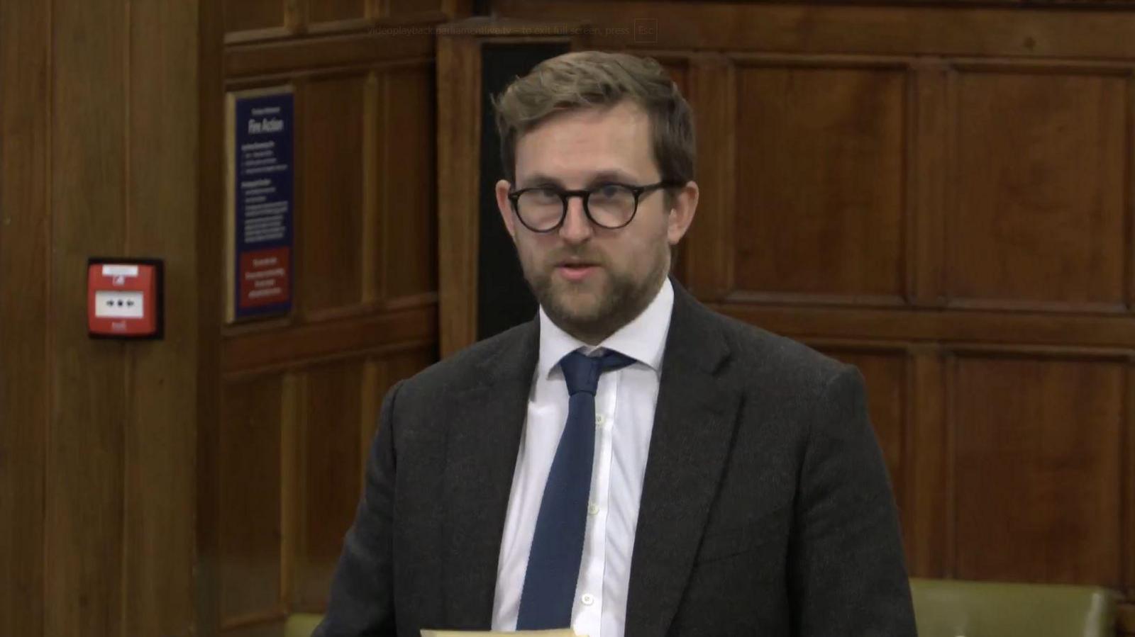 Freddie van Mierlo speaking at Westminster during the debate. He is wearing a suit and is holding pieces of paper in his hands.