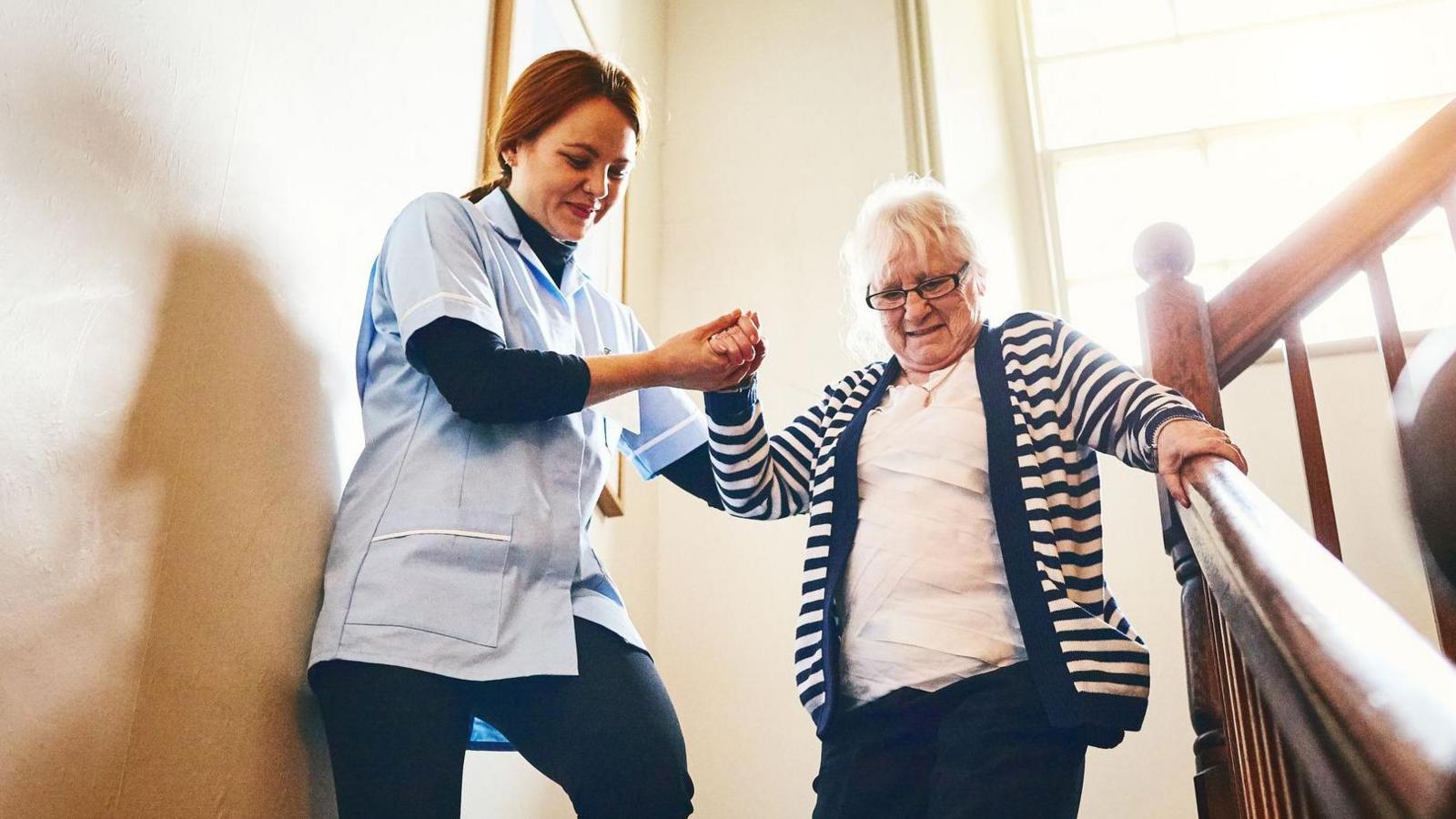 Carer helps older woman down some stairs - they are both smiling