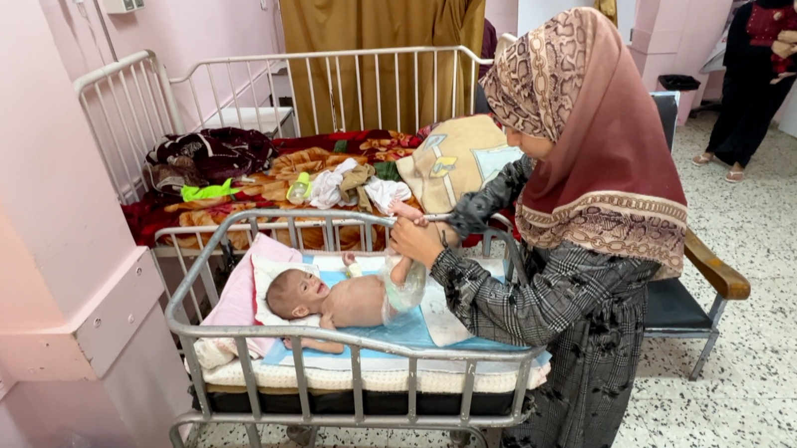 A woman in a headscarf changes the nappy of baby Siwar who lies inside a hospital cot