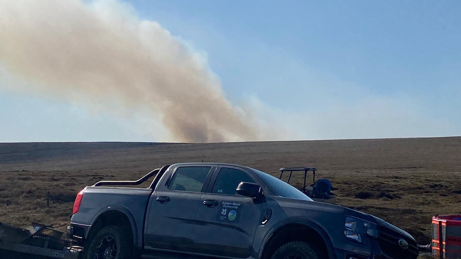 A truck near moorland in the Peak District where a plume of smoke can be seen in the distance on Friday 1 May 2026 from the wildfire off the A57 Snake Pass, near Glossop, Derbyshire.