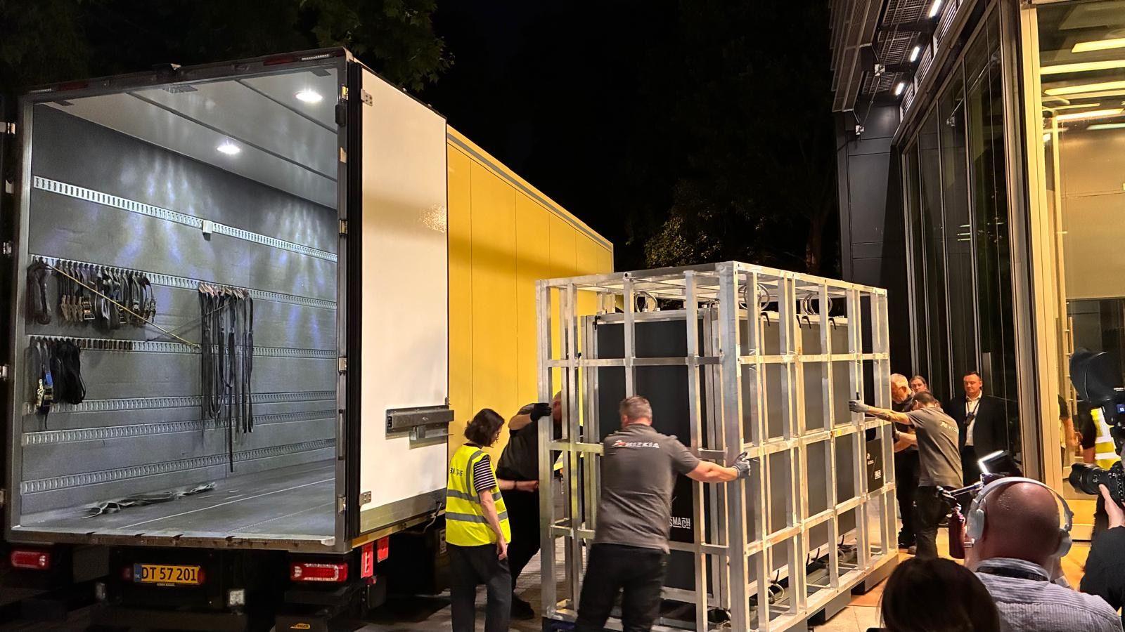 The tapestry arriving in a crate being loaded from a yellow van in the middle of the night
