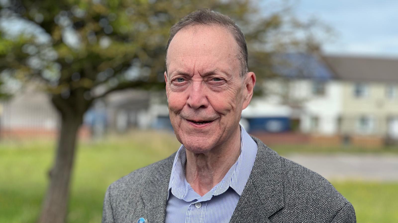 Man with grey suit and blue shirt standing outside