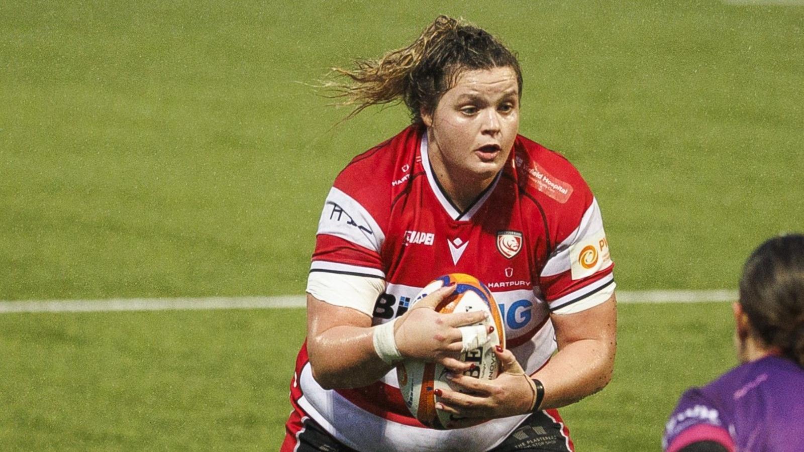 Gloucester-Hartpury back row Sarah Beckett in possession during a Premiership Women's Rugby match, wearing the red and white striped Gloucester home shirt.
