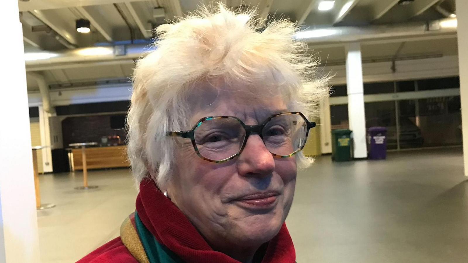 Jackie Collett, a woman with glasses and a red, yellow and green scarf looks at the camera 