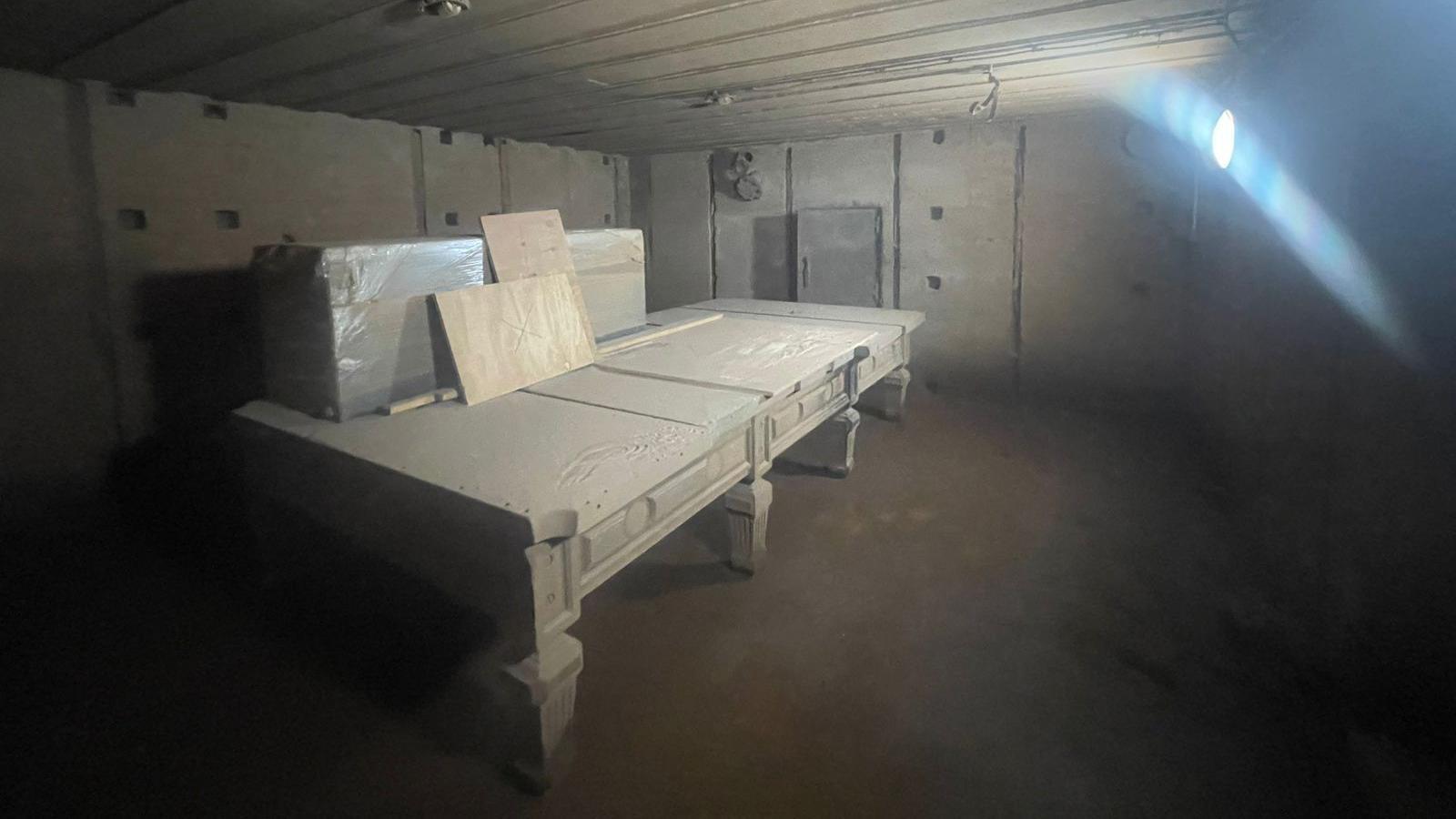 A room in a German bunker which has been sand blasted during renovation work. A snooker table covered with a sheet is in the middle of the room. It has several boxes and pieces of wood placed on top of it.