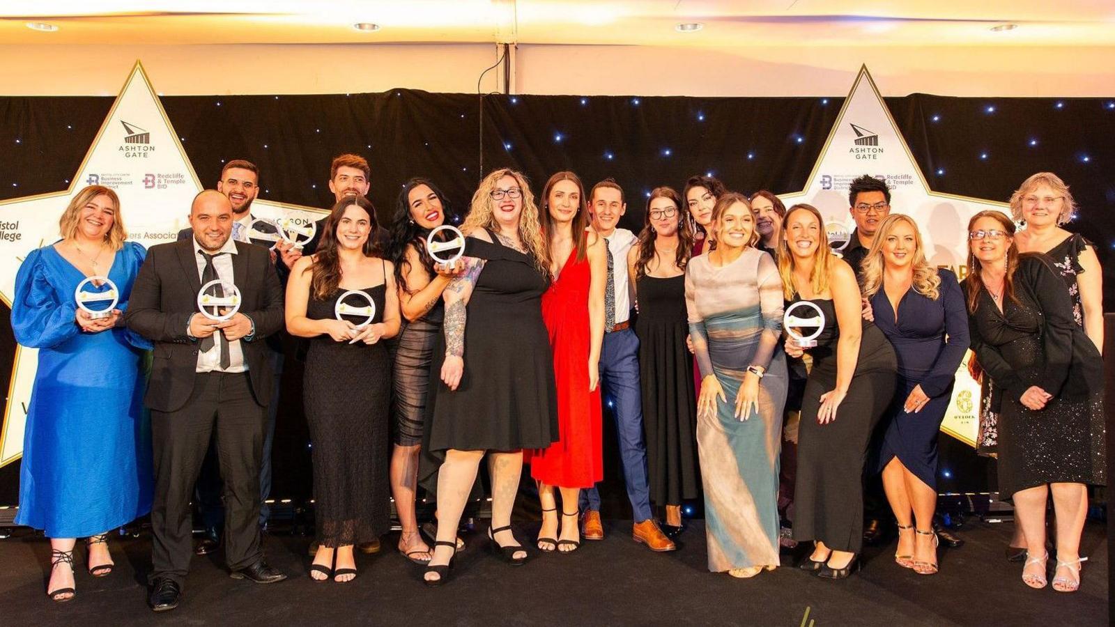 A large group of men and women, all of them in very smart outfits, pose for the camera at a hotel awards in a function room at Ashton Gate Stadium in Bristol