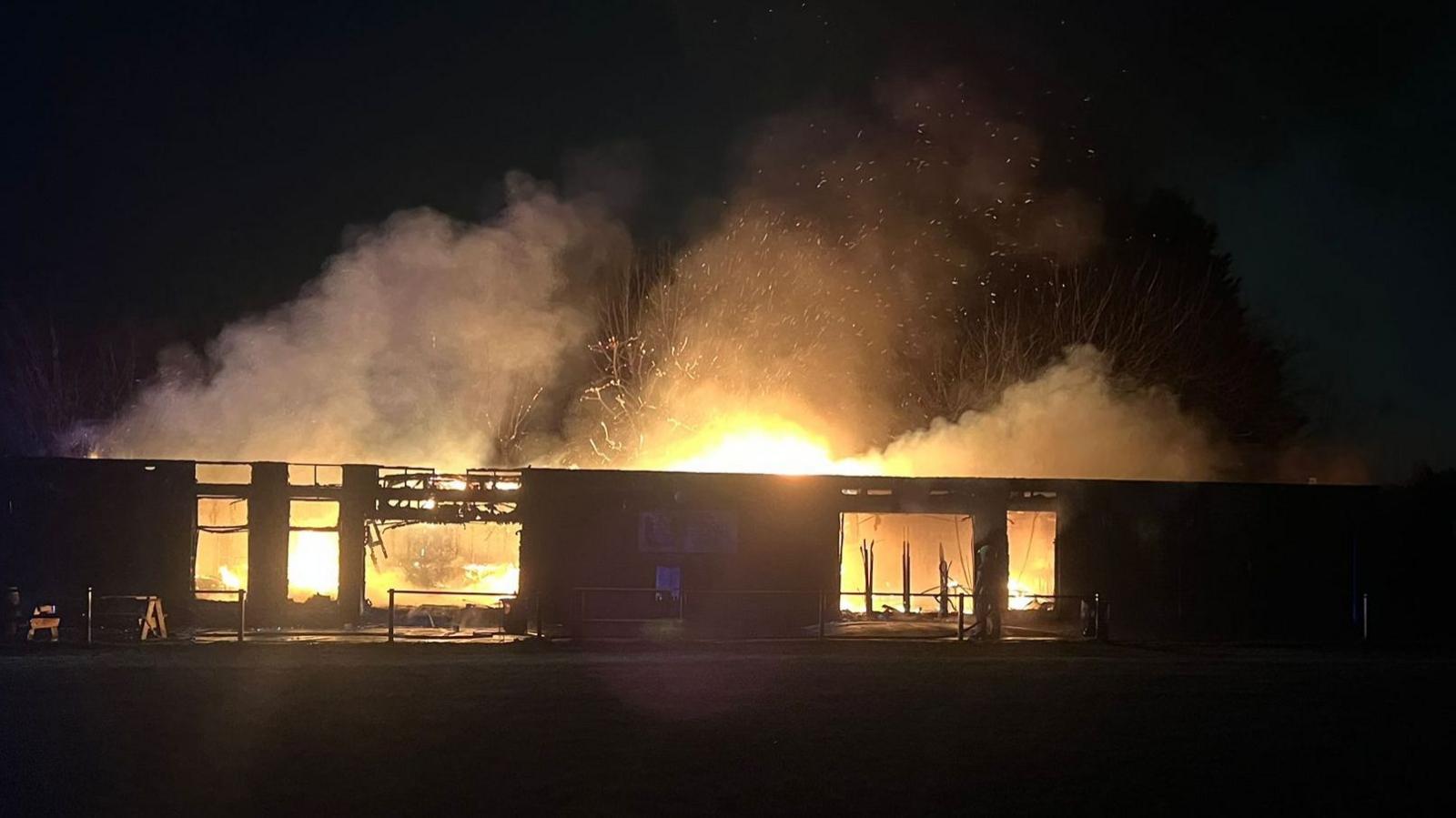 A low-rise building on fire; it is night-time and flames and smoke can be seen billowing from the clubhouse