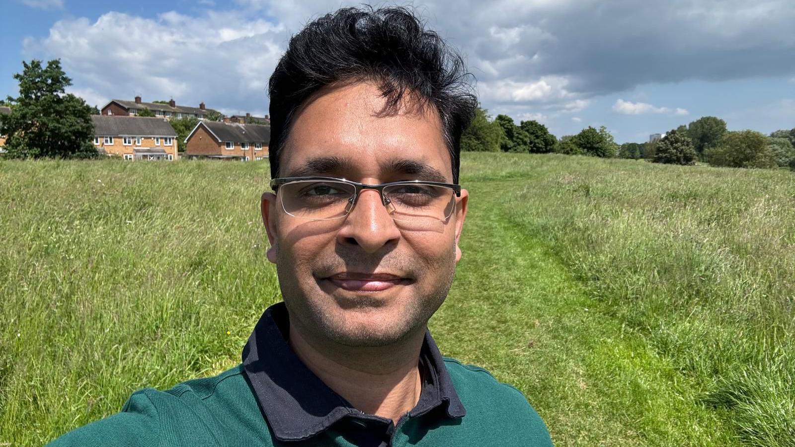 Chelmsley Wood councillor Shesh Sheshabhatter is standing in a field. He is wearing a green polo neck T-shirt and has glasses on. 