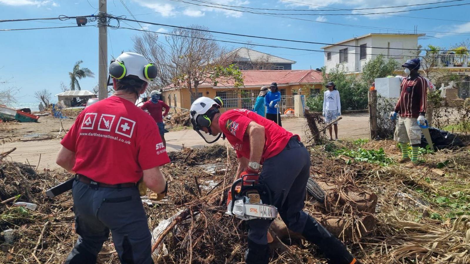 Tree surgeons with chainsaws clear fallen trees on thw hurricanw-ravaged island of Jamaica.