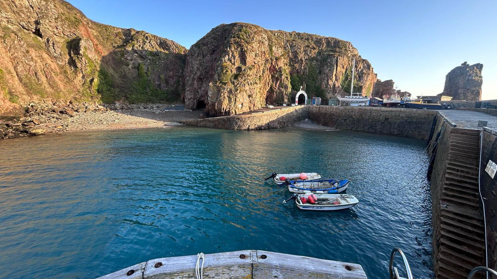 Creux Harbour in Sark. Three small boats are moored up in the harbour. A yacht is berthed on the harbour wall.