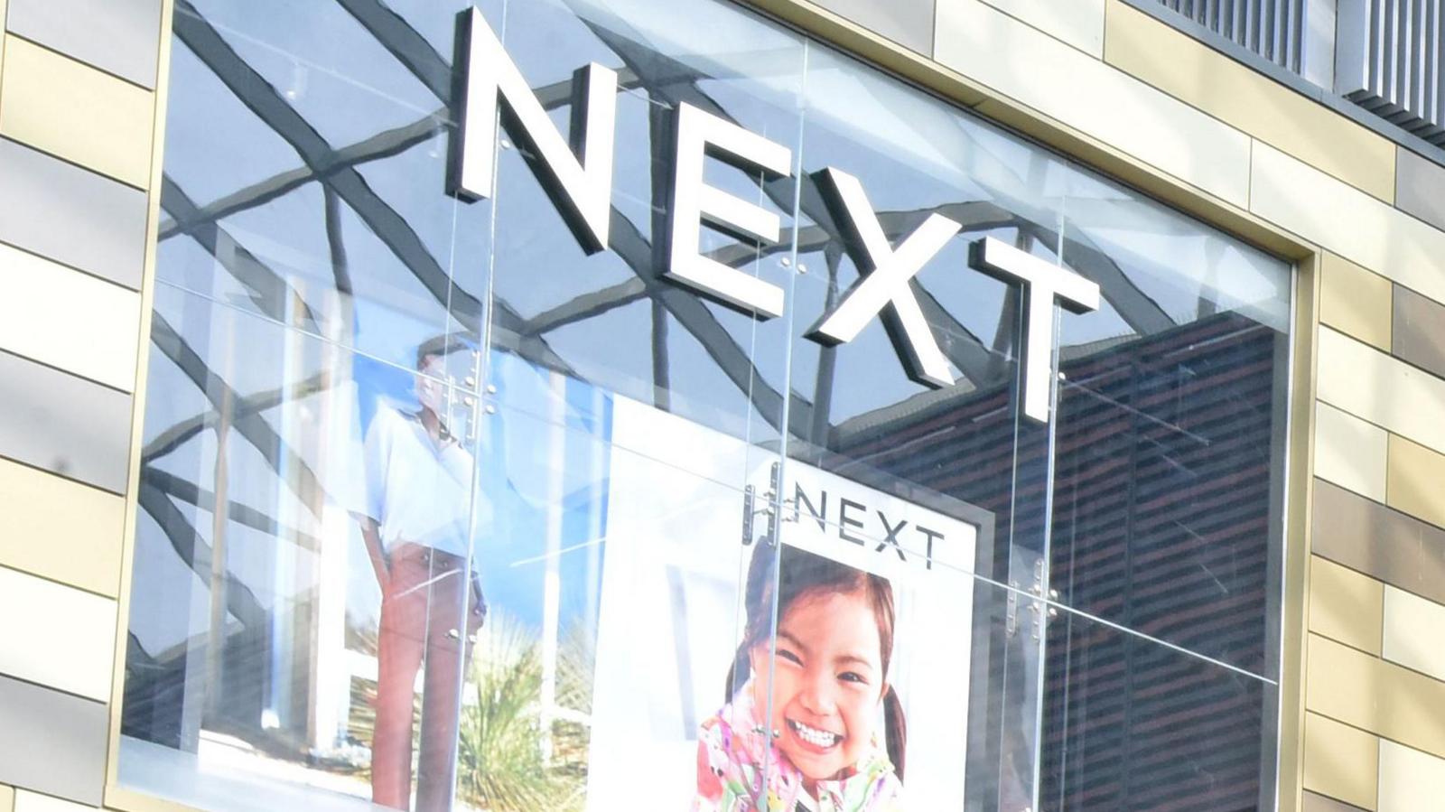 Side of a Next shop building featuring posters and the retailer's logo