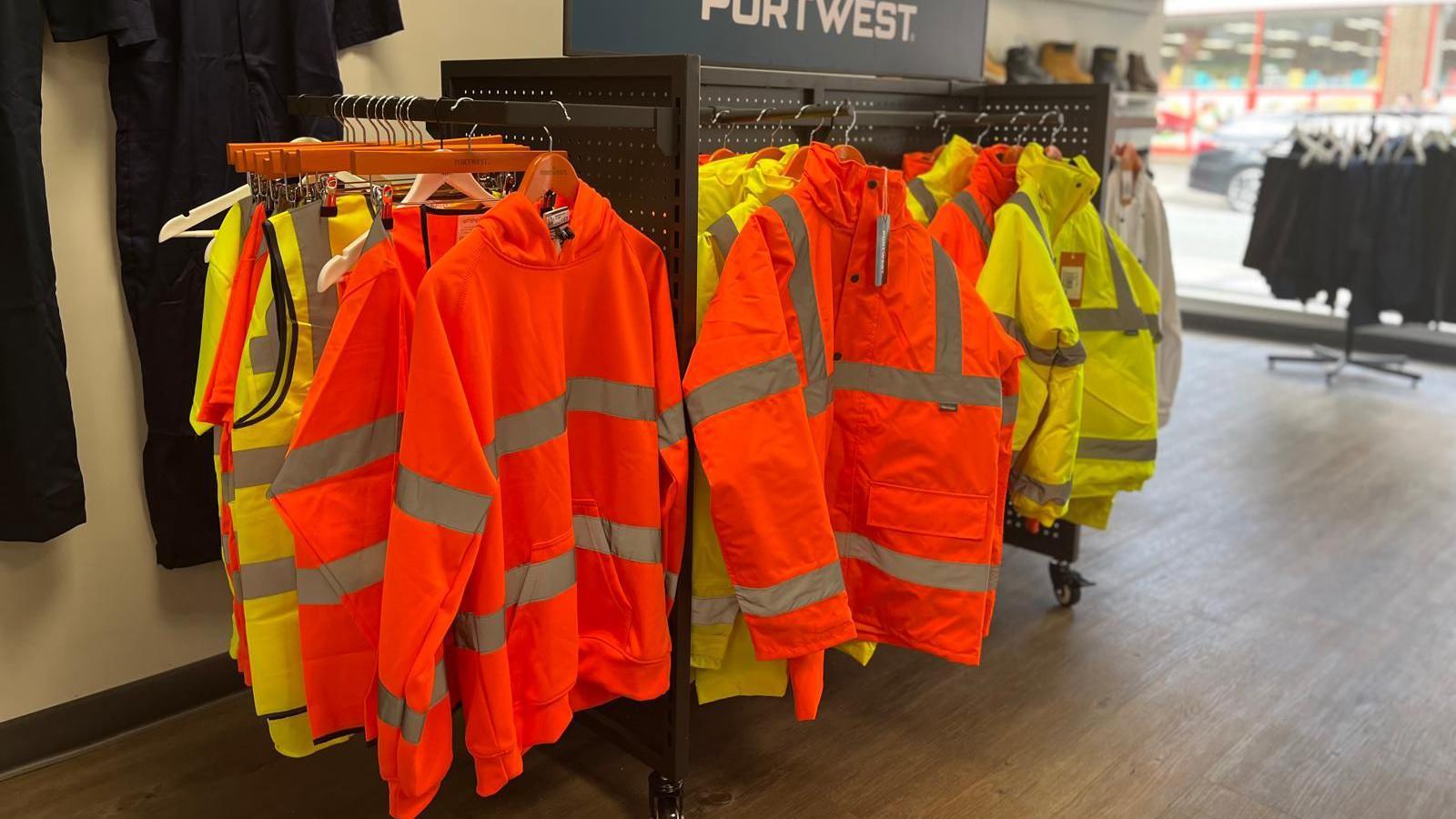 Bright orange and yellow hoodies, jackets and vests on a rail in the shop