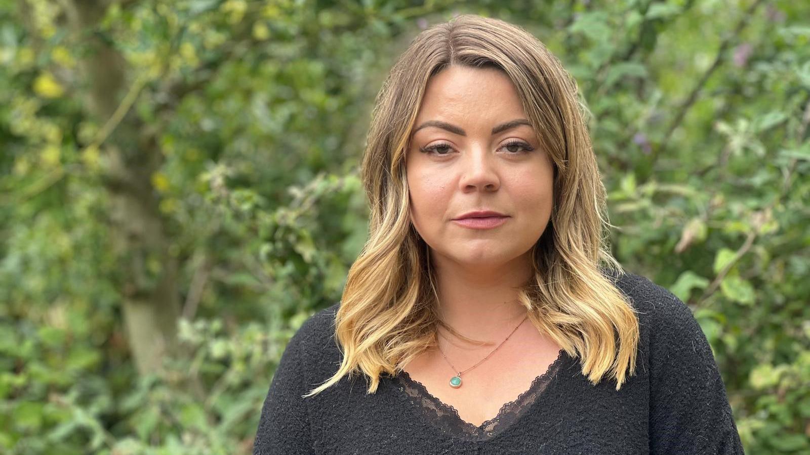 Rosie Davies looks straight at the camera. She has long blonde hair and is wearing a black top. 