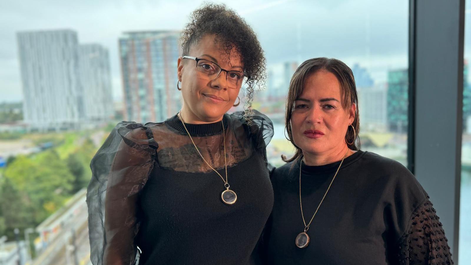 Jeannine Burke and Kelly Brown, both wearing black-tops and with necklaces holding a locket with pictures of their late sons, smile at the camera. 