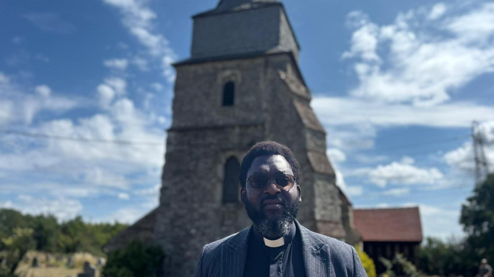A man with a clerical collar standing in front of a church