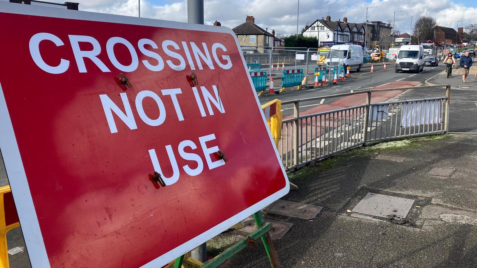 A sign indicating "crossing not in use" fills the left of the frame. Behind the sign, roadworks are in place, cones and metal barriers force the traffic into single file.