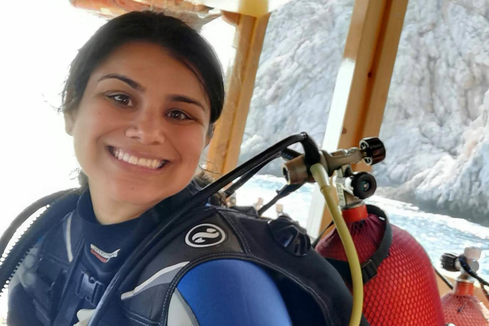 Sarah on a boat in scuba gear with cliffs visible in the background 