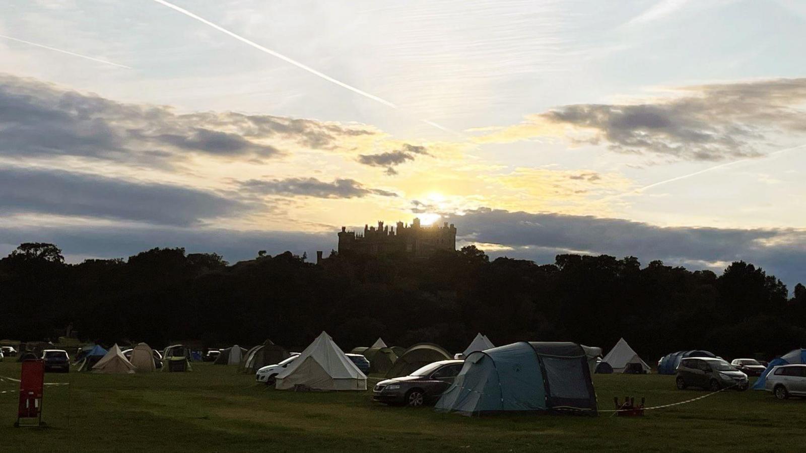 Sun rising behind Belvoir Castle with tents pitched in front