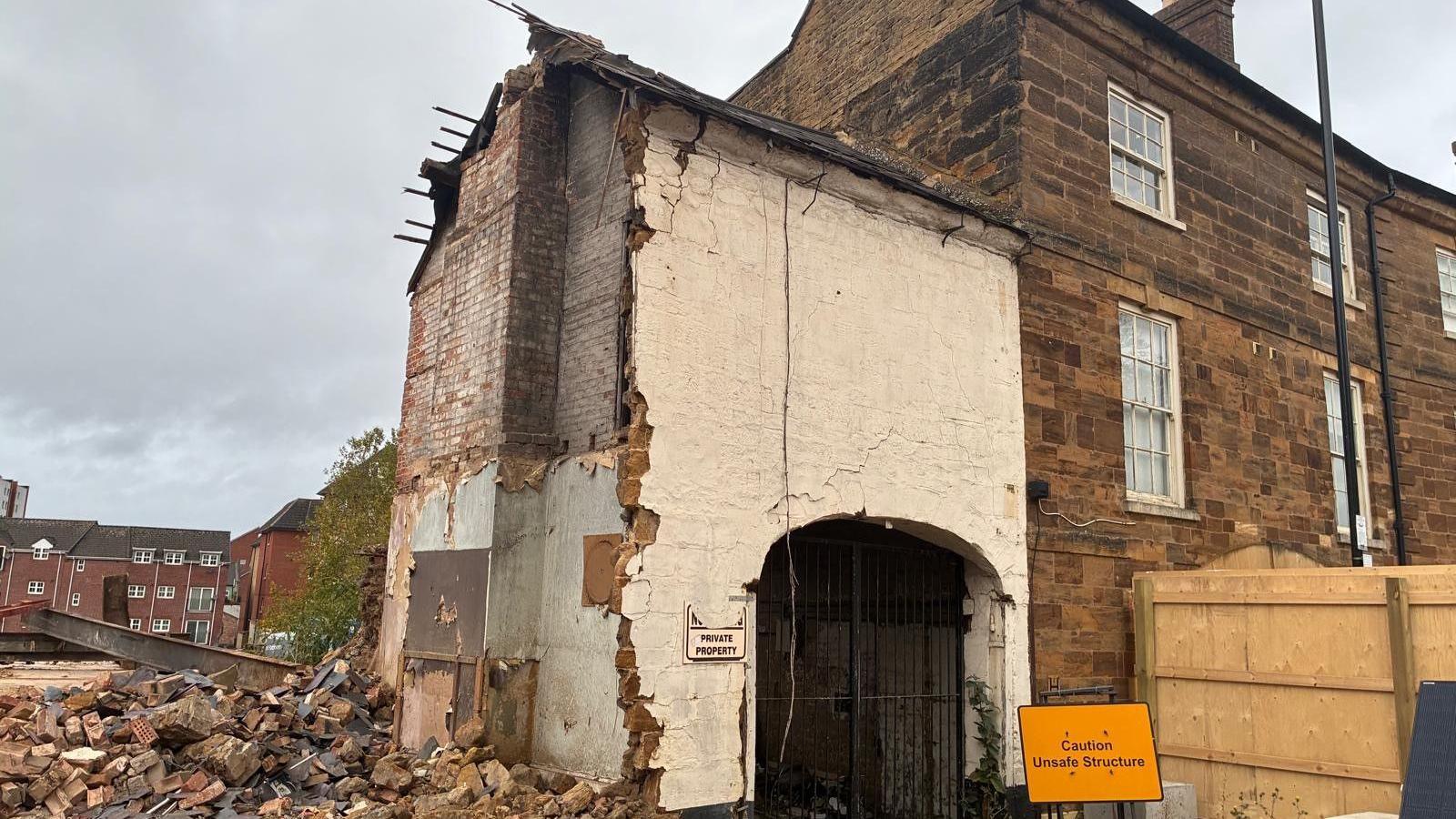 A damaged building with a white wall and black gates.