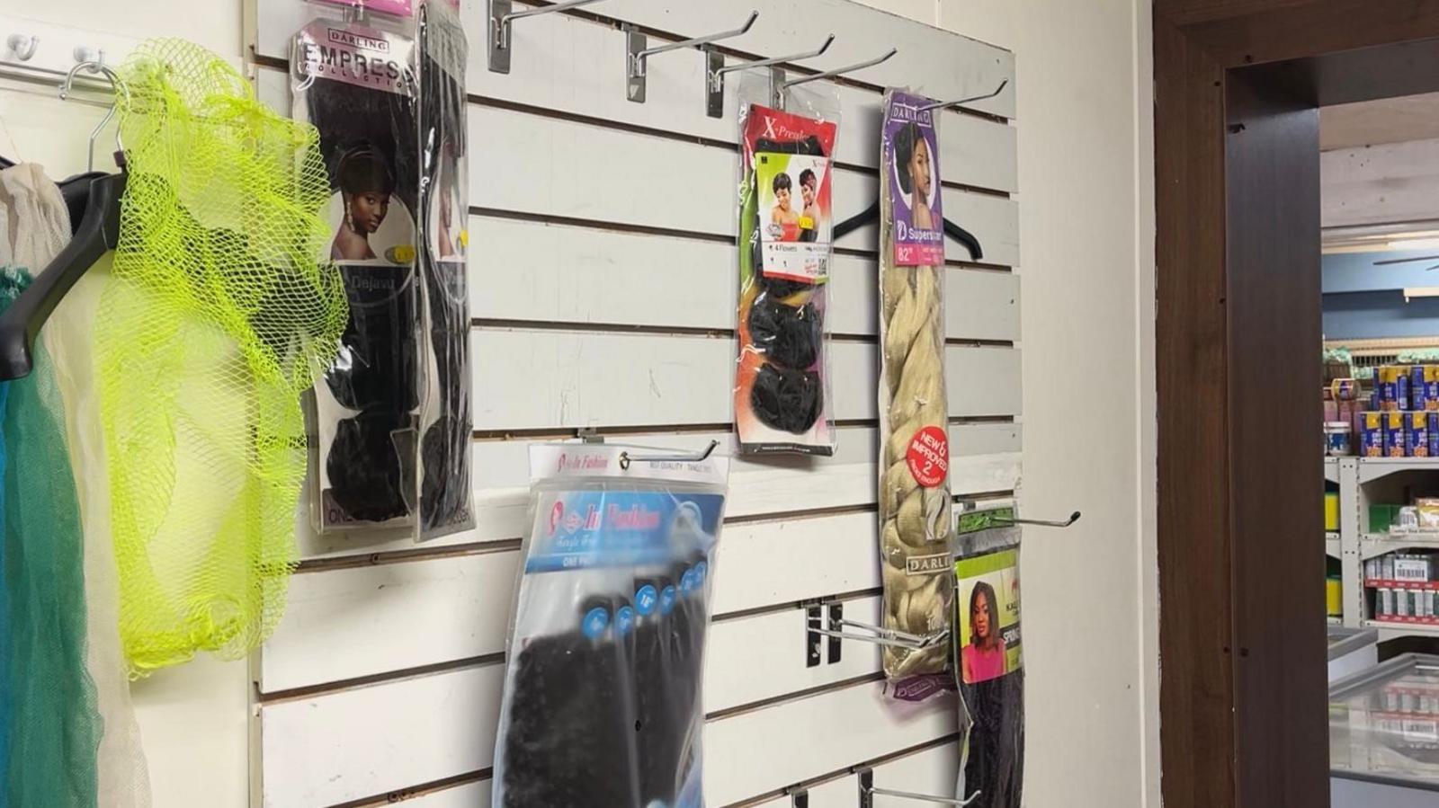 A display wall with not very many things set out on it after thieves stole much of the stock. There are empty hooks with just a few packets of hair extensions dotted around.