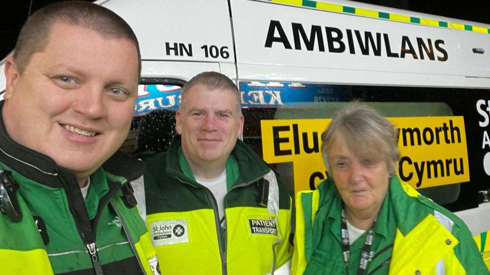 Llun o 3 gwirfoddolwr yn gwisgo siaced llachar melyn a gwyrdd, gwisg elusen St John Ambulance Cymru.