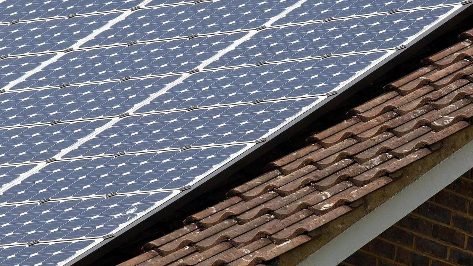 Generic image of solar panels on the roof of a building. The roof also has brown tiles on it.