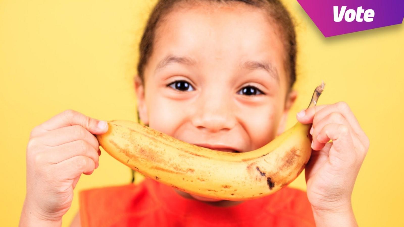 Child holding a banana up to their mouth and smiling.