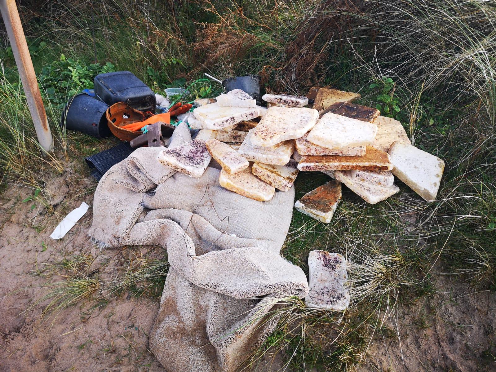 Whitish blocks of palm oils stacked up on seal grass on a beach