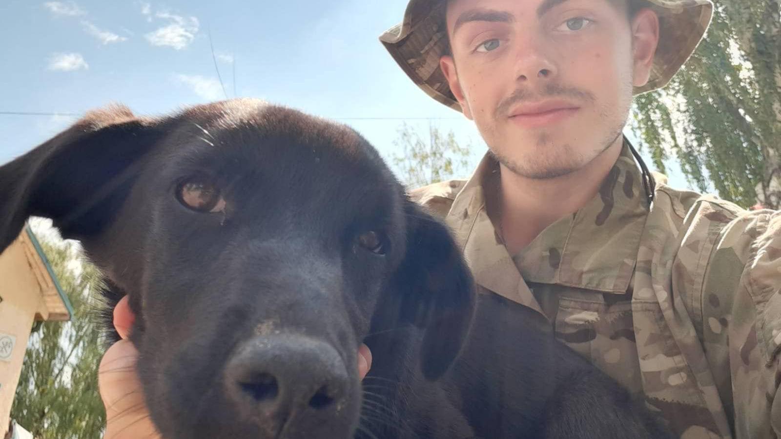 Callum Tindal-Draper wearing military camouflage clothing while holding a black dog.