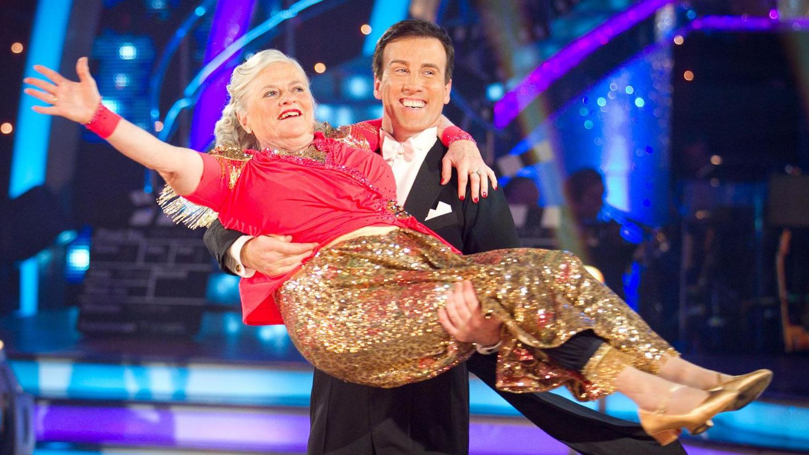 Ann Widdecombe wearing a red top and a golden glittery skirt, being held by Anton Du Beke in a tuxedo